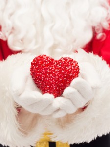 christmas, holidays, love, charity and people concept - close up of santa claus with heart shape decoration over lights background